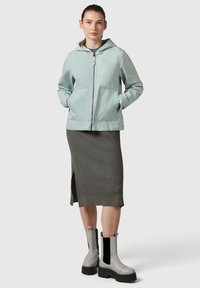 Giacca a zip blu chiaro con cappuccio, gonna grigia a coste e stivaletti Chelsea grigi con inserti elastici neri e suola spessa.