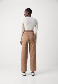 Haut ajusté à manches longues crème en côtelé et pantalon large taille haute marron à motif géométrique. Associé à des chaussures crèmes.