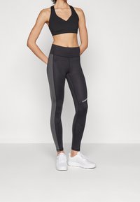 Svart sport-bh med V-ringning och högmidjade svarta tights med grå sidopaneler, i kombination med vita träningsskor.