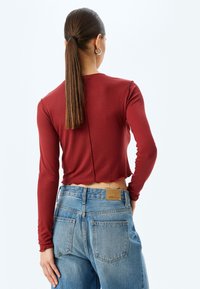 Ribbad långärmad topp i rostfärg med beskuren kant och söm bak; ihopparad med ljusblå högmidjade denimjeans med en etikett.