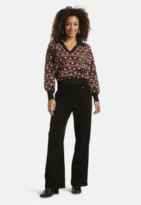 Sweater with geometric pattern in brown, cream, and black; V-neck and ribbed cuffs. Black corduroy wide-leg pants; ankle-height black boots.