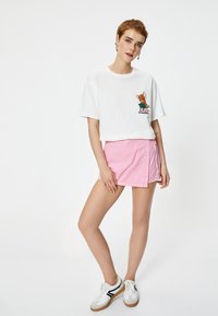 Witte cropped t-shirt met een cartoon muis graphic, gecombineerd met een roze mini rok. Model draagt witte sneakers met zwarte accenten.