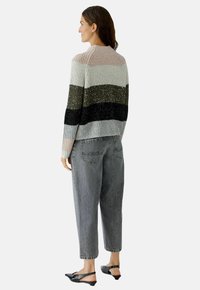 Gestrickter Pullover mit horizontalen Streifen in Hellgrau, Olivgrün, Schwarz und Puderrosa. Kombiniert mit grauen lässigen Jeans und schwarzen Slingback-Schuhen.