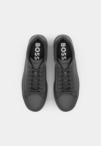 Baskets noires avec une texture lisse semblable à du cuir, bout rond et fermeture à lacets. Présente un col rembourré et un logo "BOSS" sur la languette.