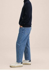 Jersey de cuello alto de punto en navy combinado con unos vaqueros de corte relajado en azul claro y zapatillas blancas con detalles en negro. Diseño simple y casual.