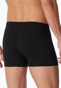 Svart bomullsboxershorts med elastisk midja och kort benlängd, med slät textur och minimala sömnadsdetaljer.