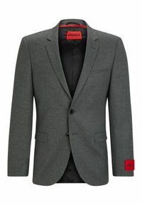 Blazer grigio su misura con due bottoni, rever a punta e fodera interna rossa. Presenta una tasca a patta e un accento rosso con marchio sulla manica.