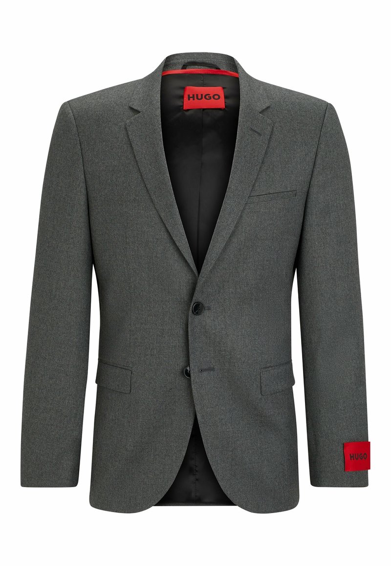 Blazer grigio su misura con due bottoni, rever a punta e fodera interna rossa. Presenta una tasca a patta e un accento rosso con marchio sulla manica.