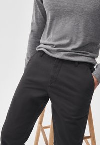 Pantaloni negri dintr-un material neted, cu buzunare laterale și un design ajustat, asortați cu un top din tricot gri cu mânecă lungă.