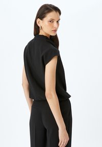 Sort ærmeløs top med et cropped design, lavet af tekstureret stof. Har en rund halsudskæring og lette skulderpuder.