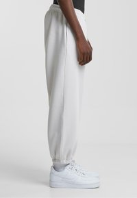 Hvide sweatpants med elastiske manchetter, sidelommer og snor i taljen, parret med hvide sneakers. Glat, blødt stof.