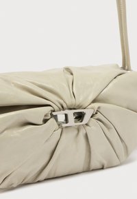 Ανοιχτό μπεζ τσάντα από δέρμα με ρυτίδες, κούμπωμα ασημί και λεπτό λουρί ώμου πάνω σε λευκό φόντο.