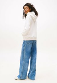 Felpa bianca con cappuccio, in tessuto morbido, con vestibilità rilassata, abbinata a jeans blu a gamba larga, con lavaggio chiaro e design classico a cinque tasche.