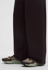 Sneakers met een mix van beige en bruine materialen, gaasdetails en een gestructureerde rubberen zool, gedragen met losse, donkere broeken.