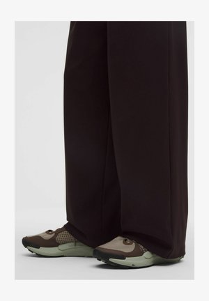 Sneaker mit einer Mischung aus beigen und braunen Materialien, Netzdetails und einer strukturierten Gummisohle, getragen zu locker sitzenden dunklen Hosen.