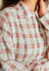 Let skjorte i tern i lyserøde, hvide og beige nuancer. Har en klassisk krave, knaplukning og tekstureret stof med en blød finish.