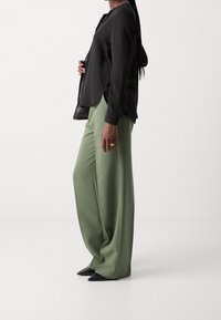 Blusa nera a maniche lunghe abbinata a pantaloni larghi di un verde chiaro e décolleté neri a punta. Tessuto morbido e forma rilassata.