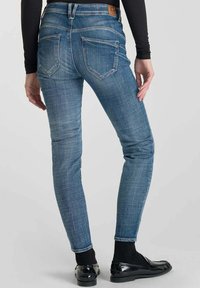 Jeans en denim bleu skinny avec une taille mi-haute. Comprend cinq poches, des coutures discrètes et un patch en cuir de la marque au dos de la taille.