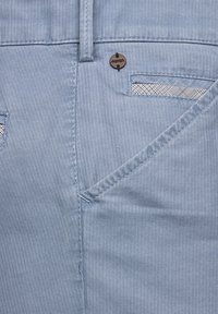 Light blue trousers featuring vertical stripes, a front pocket with a plaid accent, and a round logo tag near the waistband.