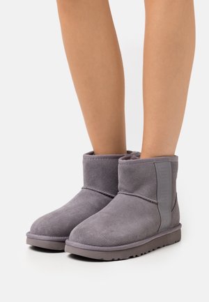 Bottines en daim gris avec un bout arrondi et une surface douce et texturée. Elles présentent un accent de marque sur le côté et une semelle en caoutchouc.