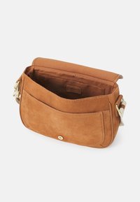 Borsa a tracolla in suede beige con chiusura a pattina, tracolla in tessuto, tasca frontale e interno liscio. Presenta un dettaglio con bottone dorato.