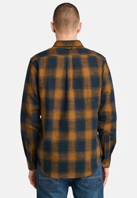 Langsleeve geruite shirt in marineblauw en verbrande sinaasappel, voorzien van een button-down kraag, borstzak en een textuurstof met een geruit patroon.