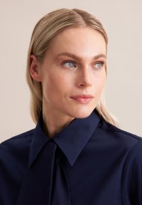 Navyblauwe blouse met een puntige kraag, met een gestrikt detail aan de voorkant; gladde textuur en gestructureerd ontwerp.