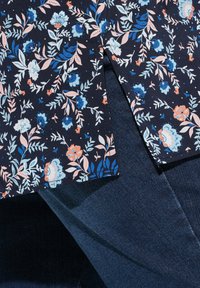 Bloemenblouse met een marineblauwe achtergrond, versierd met blauwe, roze en witte bloemen. Gepaard met donkere denimjeans, wat een casual, gelaagde look laat zien.