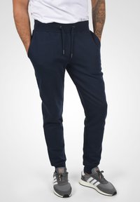 Marina joggers med elastisk midja, justerbar dragsko, sidofickor och smal passform, ihop med grå träningsskor.