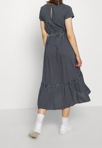 Abito midi a righe navy con maniche corte a sbuffo, vita elastica e gonna a strati. Presenta un'apertura a occhio di pernice sul retro.