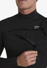 Neopreno negro con cremallera y detalle de gancho en el pecho. Presenta un material suave y elástico y costuras planas para mayor durabilidad.