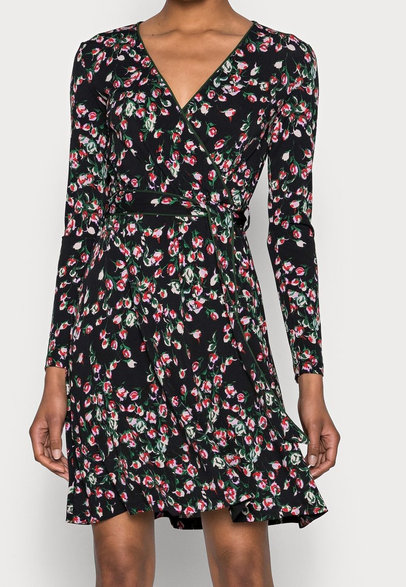 Robe noire portefeuille à manches longues avec un motif floral composé de petites fleurs rouges, blanches et vertes, nouée à la taille.