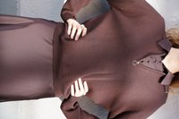 Brauner Strickpullover mit einem Reißverschluss-Mock-Kragen, glatter Textur und langen Ärmeln. Kombiniert mit einem passenden, fließenden braunen Rock.