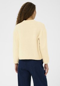 Pull léger beige fait de matériau doux, doté de manches longues et d'un col rond, associé à un pantalon en denim foncé.