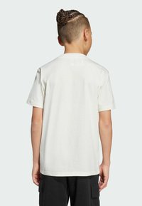 Crewneck-T-Shirt aus leichtem cremefarbenem Baumwollstoff, kurze Ärmel, weiche Textur, mit lässigem Schnitt. Getragen mit schwarzen Cargo-Hosen, Rückansicht gezeigt.