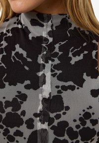 Top cu guler înalt, cu un model în culori negre și gri, având o textură din plasă, cu un design abstract cu pete și detalii cu cusătură centrală.