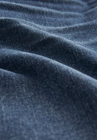 Close-up of dark blue denim fabric with visible weave texture and soft folds creating gentle waves and shadows.