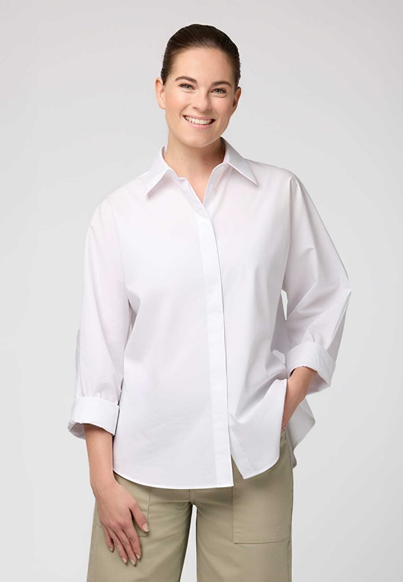 Camicia bianca con colletto a punta, maniche arrotolate e vestibilità rilassata. Realizzata in un tessuto morbido, presenta un orlo dritto.