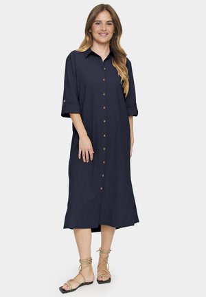 Abito blu navy con bottoni, maniche a tre quarti, caratterizzato da bottoni in legno e una silhouette fluida che scende sotto le ginocchia. Tessuto morbido.
