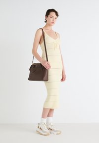 Lys gul strikket kjole med horisontale striber, parret med en brun handbag med tekstureret top-håndtag og guld-accenter.
