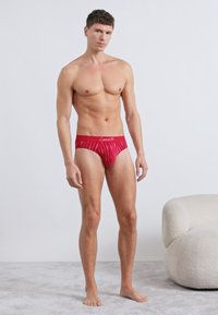 Piros férfi alsónadrág fehér vonal mintákkal, rugalmas derékpánt "Love" felirattal, testhezálló kialakítás, sima anyag, további díszítések vagy részletek nélkül.