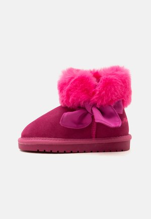 Petite botte rose foncé avec un bord duveteux rose vif et un grand ruban noué sur le côté, semelle plate, vue de profil.