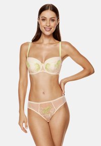 Beżowy zestaw bielizny z wyściełanym biustonoszem na drucie, ozdobionym zielonym haftem kwiatowym oraz pasującymi przezroczystymi majtkami. Ramiączka są w jasnym zielonym kolorze.