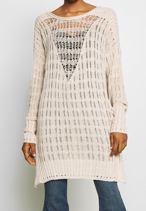 Pull en tricot beige avec un large tissage, décolleté en V, manches longues et ourlet côtelé, présentant des motifs ajourés sur l'ensemble.