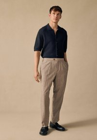 Camisa de manga corta texturizada en color marino, pantalones rayados claros con pliegues y zapatos negros. Fondo neutro con iluminación suave.