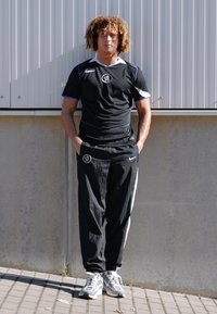 Sort atletisk skjorte med blå accenter, sorte bukser og grå sneakers. Skjorten har et logo på brystet og hvide detaljer.