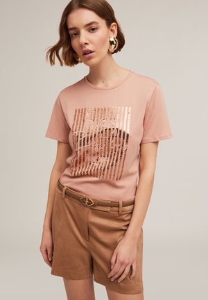 Light pink t-shirt with a sequined graphic reading "Paris Amour" in silver and rose gold, paired with beige shorts and a golden belt buckle.