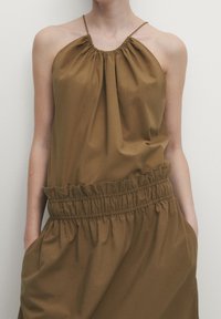 Robe marron à bretelles spaghetti avec une taille élastique, un corsage froncé et des poches latérales. Tissu lisse avec une coupe détente.