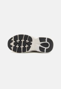 Svart gummisåle med fleksibel design. Har teksturerte gripe mønstre og en hvit mellomsåle for demping. Merkevaren er synlig.