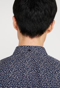 Námořnická květinová košile s malými, barevnými tečkami. S límečkem, obsahuje knoflík a texturovanou tkaninu, vhodná pro neformální nošení.